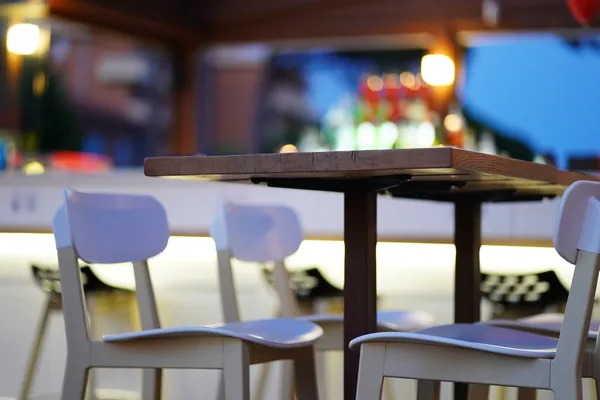 Holztisch und weiße Stühle im Café vor unscharfem Barbereich