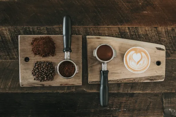 Kaffeebohnen, Siebträger mit gemahlenem Kaffee und Latte mit Herzmotiv auf Holzbrettchen